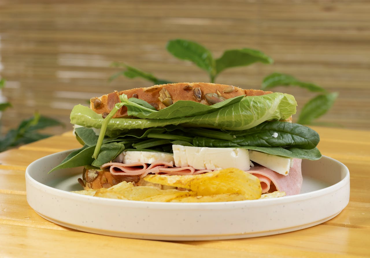 about-us Mouthwatering sandwich with fresh spinach, ham, cheese, and crispy chips on a plate.